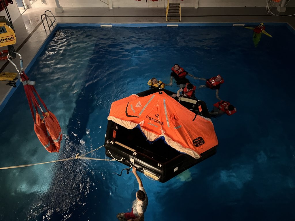 Delegates creating a ring by linking their arms and floating in the pool, helping each other to enter the life raft | MSA Dover STCW Basic Safety Training Week